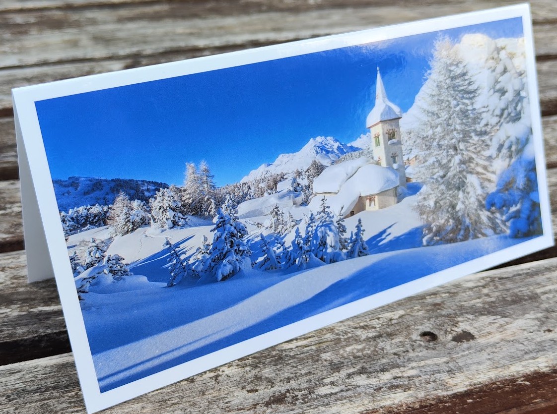 Panoramakarte im DIN lang Format mit verschneiten Bäumen und Kirche in den Bergen bei blauem Himmel.
